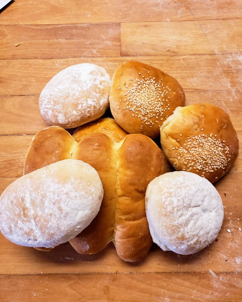 A pile of fresh baked buns and rolls on a floured wooden counter