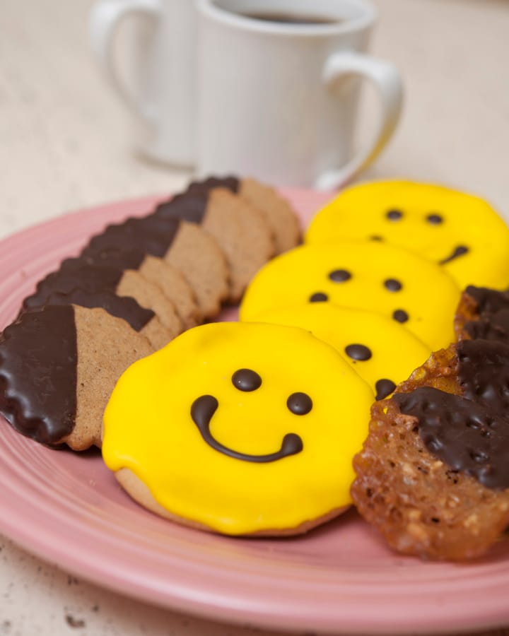 Smiley face cookies and chocolate dipped shortbread on a plate with coffee